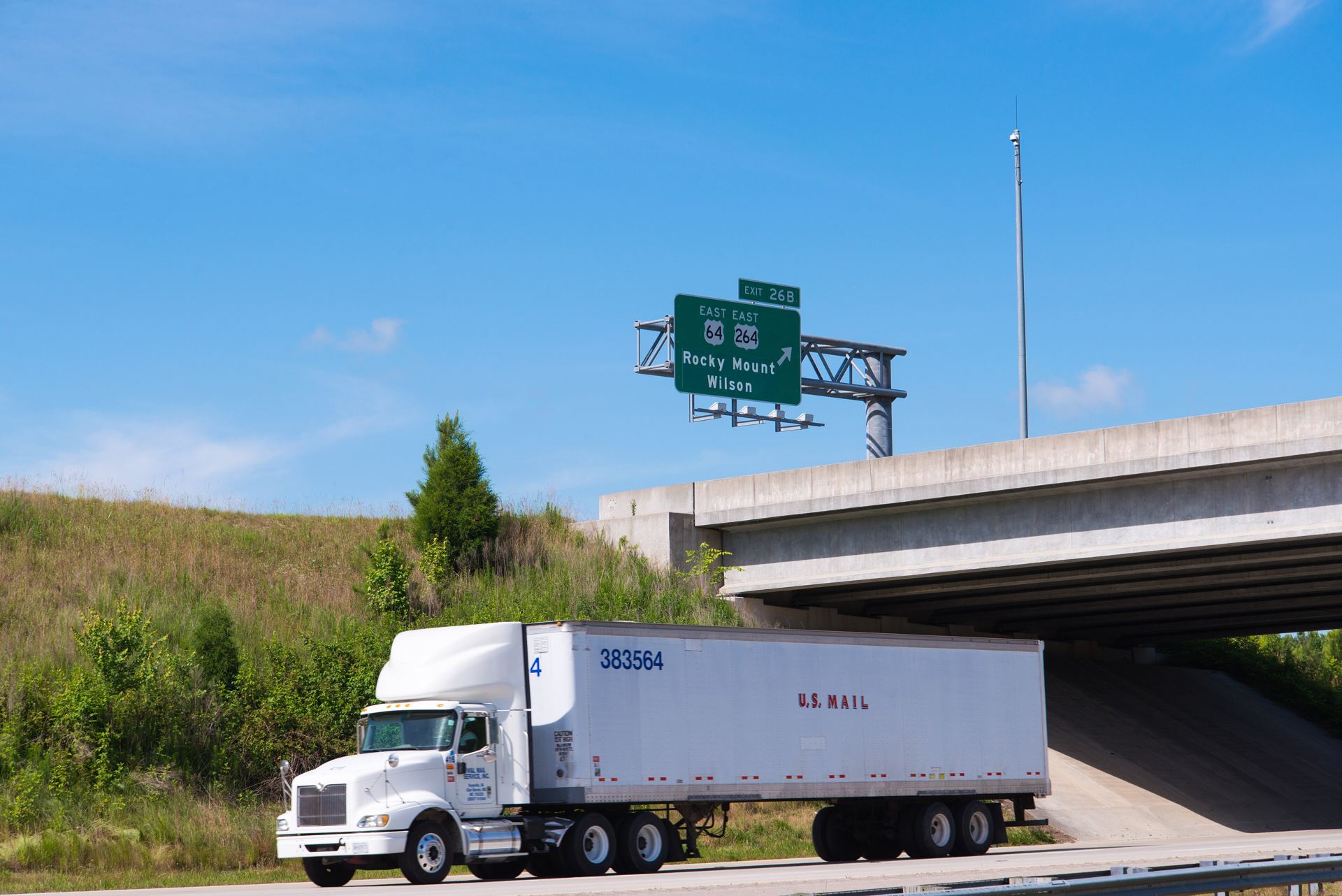 A truck on an interstate ramp under an overpass, with an exit sign above