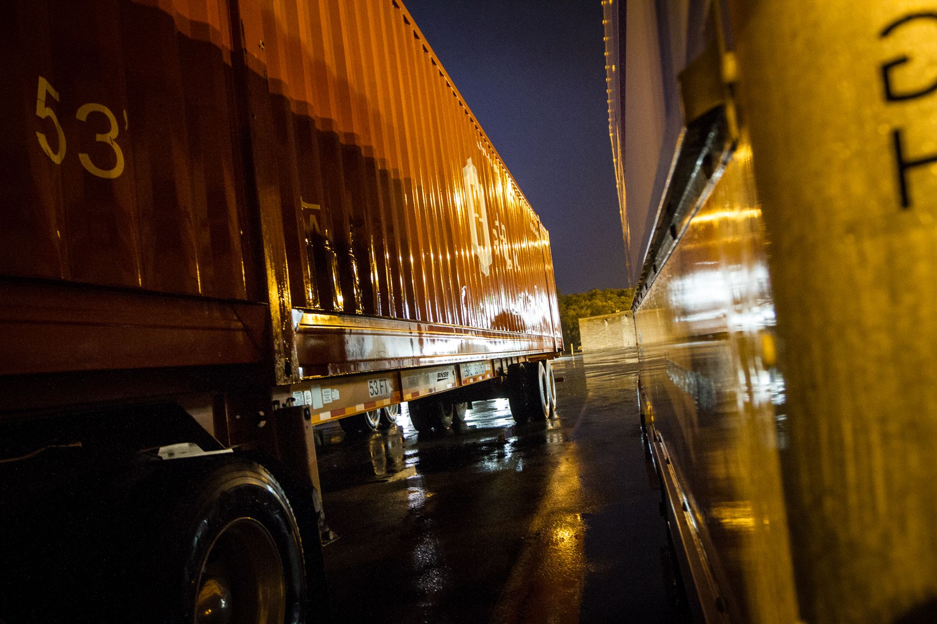 Trailers parked side by side at a truck stop on a rainy night